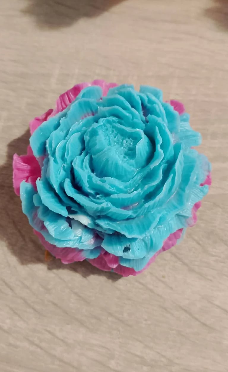 Turquoise and pink paper flower with layered petals on a white wooden surface