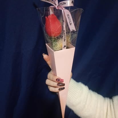 Person holding a wrapped bouquet with a single red rose and green foliage