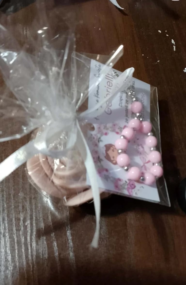 Two cellophane gift bags on wooden surface: one with beige frosting cupcake and white bow, one with pink pearl beads and decorative card