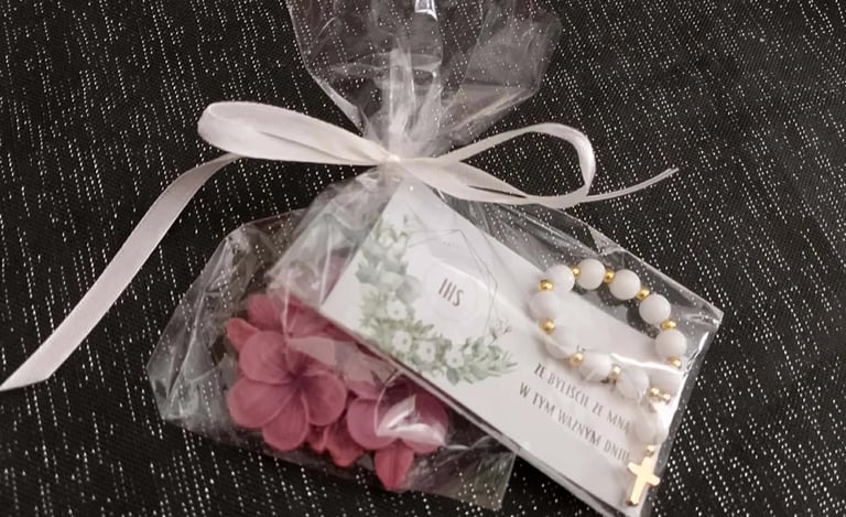 Organza gift bag with pink petals, beaded bracelet, and decorative tag tied with white ribbon on dark textured background