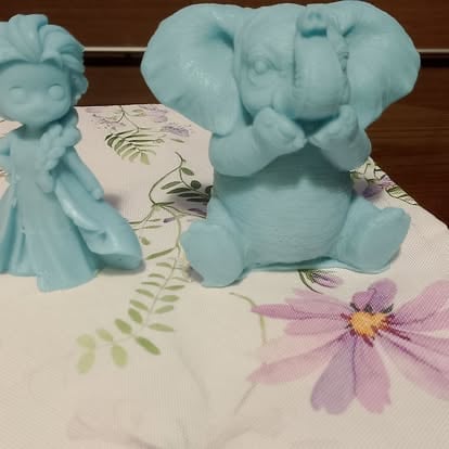 Two light blue decorative elephant figurines on floral patterned paper with painted flowers and ferns